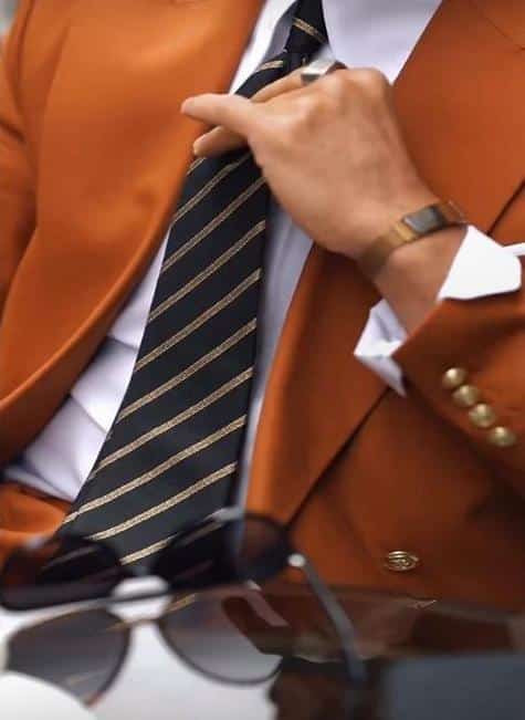 Homme ajustant sa cravate avec un blazer orangé élégant